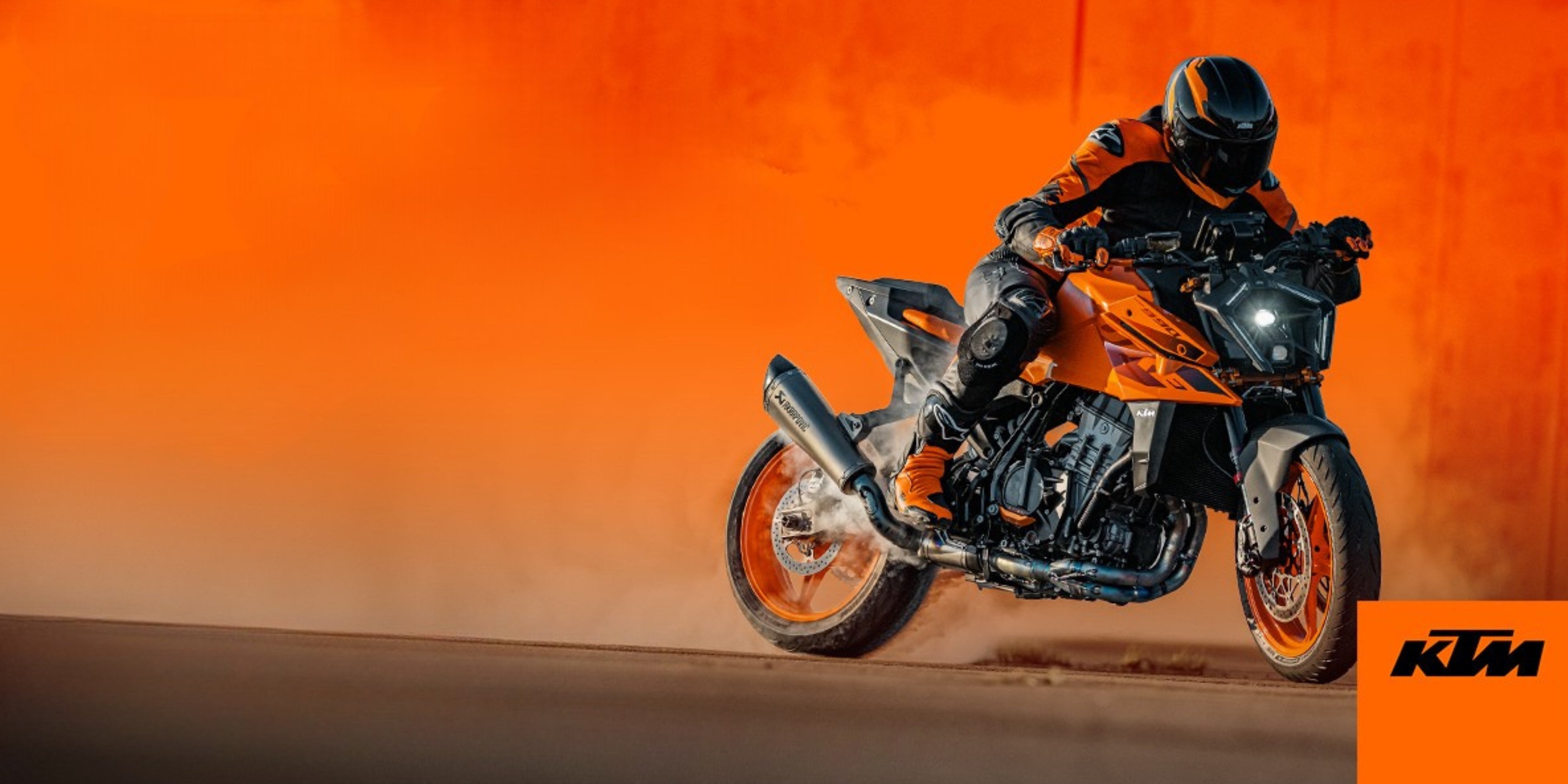 Motorcyclist riding an orange and black KTM bike on a desert track with an orange background