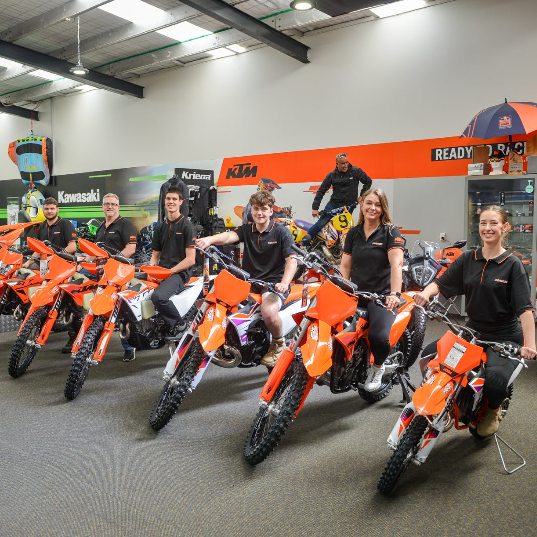 Makz Gear Team posing with orange KTM dirt bikes in a showroom.